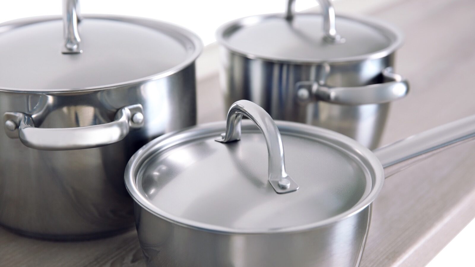 Trois casseroles en acier inoxydable avec leur couvercle sur un plan de travail