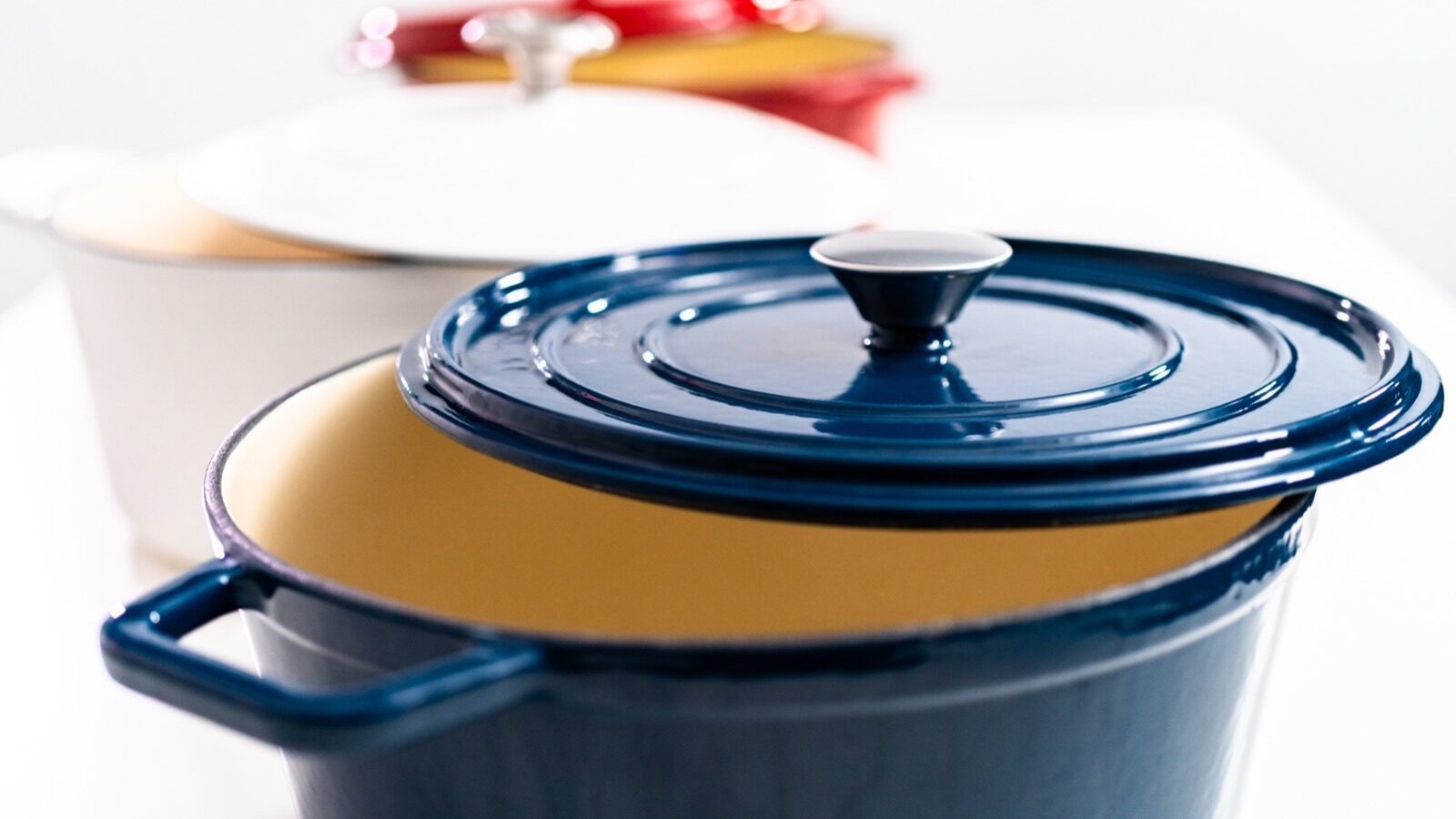 Trois cocottes rondes en fonte émaillée bleue, blanche et jaune posées sur fond clair