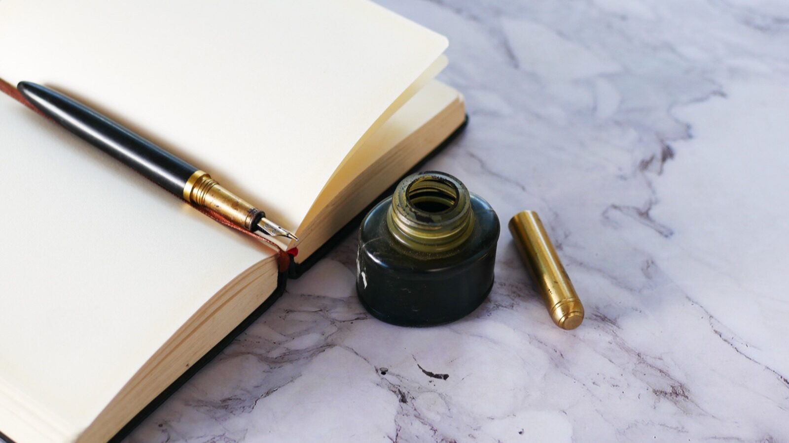 Stylo plume posé sur un carnet ouvert à côté d'un encrier en verre